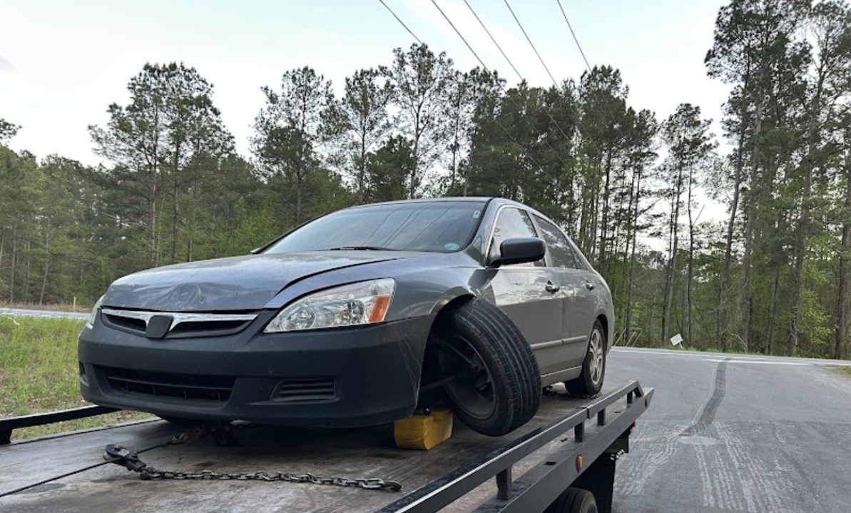 A damaged sedan secured on the flatbed with a wheel chock