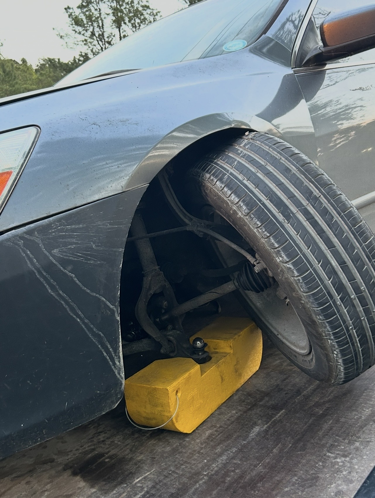 A yellow wheel chock holding a damaged front wheel secure on the flatbed